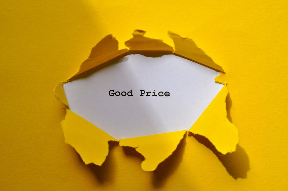 A torn piece of yellow paper with rough, irregular edges revealing a white inner layer that is folded outward. Inside the torn opening, there is a piece of plain white paper with the handwritten phrase 'Good Price' in black ink. The torn yellow paper contrasts with the smooth white paper and the background, which is also yellow, creating a visually striking image. The scene suggests themes of packaging, deals, or pricing related to house removals or moving services, in line with the context provided by Man with Van Ratcliff's services and the webpage topic on relocation costs.